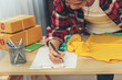 © aFotostock - Fashion designer Women measure clothing design packing box on table. Women checking goods size, quality to delivery box package. Entrepreneur Asian woman startup small business at home office desk