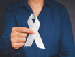 © meeboonstudio - Close-up of hand holding a white ribbon on a gray background
