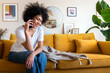© Daniel - Happy African American woman on mobile phone call sitting at home couch. Copy space.