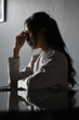 © bongkarn - Stressed and depressed Asian businesswoman at her desk in the dark office room