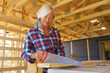 © Halfpoint - Senior woman sawing wood board inside of her unfinished ecological sustainable wooden eco house. Concept of active independent women and seniors, eco house and healthy lifestyle.