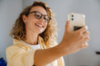 © Drobot Dean - Young beautiful smiling curly woman in glasses taking selfie