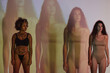 © Clique Images - Horizontal medium long shot of two ethnically diverse women in underwear standing in projector light with repeating image of one of them