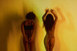 © Clique Images - Horizontal back view view medium long studio shot of two young women wearing underwear standing in yellow projector light