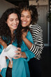 © Clique Images - Vertical medium portrait of two happy young women in love standing together in kitchen and hugging while one of them washing dishes