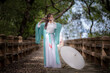© APchanel - Young beautiful asian woman wear dressing in traditional Chinese costume ancient fashion style with bamboo flute music on hand travel in nature outdoor with green nature of park background.