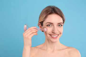 Canvas Print - Young woman using natural rose quartz face roller on light blue background