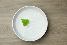 White Bowl With Water And Green Leaf On Wooden Table, Top View