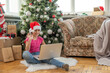 © Angelov - Christmas tree in a large living room. Little girl plays near the Christmas tree. A girl with a laptop communicates with friends