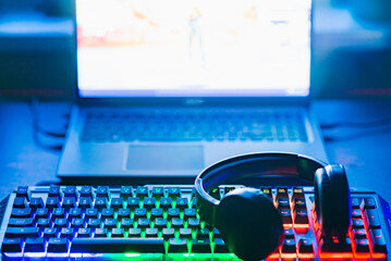 Wall Mural - Pro gaming illuminated desk, headset, keyboard, computer neon lights. Cyber sport equipment laying on desktop, ready for online video gaming.Dark shot.