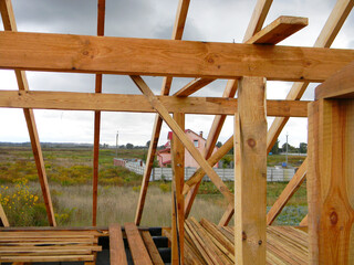 Wall Mural - Wood framing during the roofing construction.Timber trusses, roof framing with a close-up of roof beams, struts and rafters against a cloudy rainy weather.