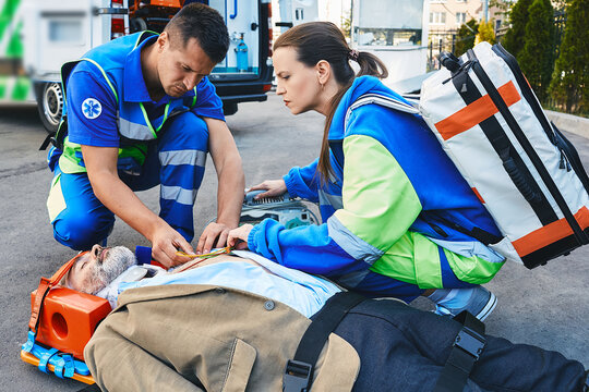 Two paramedics helping injured patient lying on stretcher and installing sensors on his chest to monitor his heart health with medical equipment. Ambulance personnel