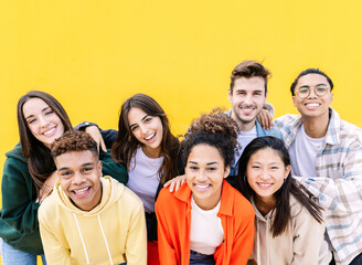 Wall Mural - Group portrait of young multiethnic student friends against yellow wall - Diverse united millennial boys and girls smiling at camera outdoors - International youth community people concept