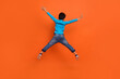 Full length photo of adorable small boy jumping back view spread legs arms dressed stylish blue clothes isolated on orange color background