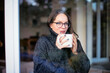 © sepy - Smiling woman standing by the window and drinking tea