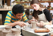 © FotoArtist - Close-up of concentrated beautiful craftswoman in apron sitting at pottery wheel and using craft tool while shaping wet clay vessel