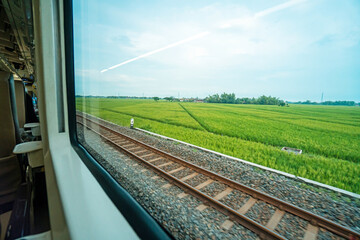 Riding a train in Indonesia sitting by the window watching the tracks and the view outside the window of the train speeding towards its destination