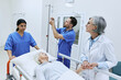 © Peakstock - Nurse putting drip on elderly patient lying on gurney while being examined by experienced woman doctor. Medical assistants will take injured woman to her medical ward