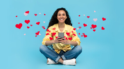 Wall Mural - Young lady using smartphone, chatting online with friend, surfing internet, watching video, blue background