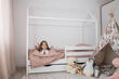 © sofiko14 - Portrait of a beautiful caucasian little girl smiling while relaxing in her bedroom during a leisure day. Cheerful female kid lying on scandinavian wooden house frame bed.