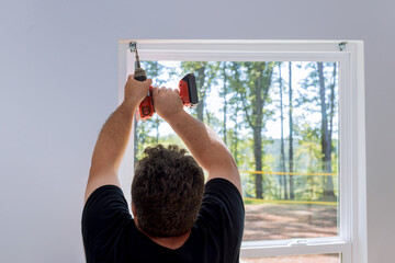 This is professional technician installing blinds on windows of newly constructed home by screwing the fasteners in