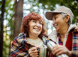 © Raisa Kanareva - Two elderly woman friends walk in the forest, pour coffee from a thermos, have a great time together, an elderly happy couple.