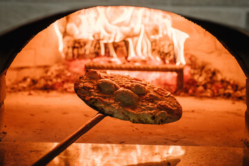 Wall Mural - The chef takes a baked pizza Margherita, four cheese or meat pizza from the oven. A cooking and baking pizza in a firewood oven. Italian traditional pizza is cooked in a stone wood-fired oven.