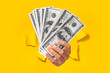Female hand holding fan of cash money in dollar banknotes, isolated through torn yellow background, closeup