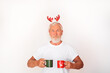 Portrait of a mature grey-bearded man wearing a white t-shirt and Christmas antlers, holding mugs, on a white studio background. Christmas time concept