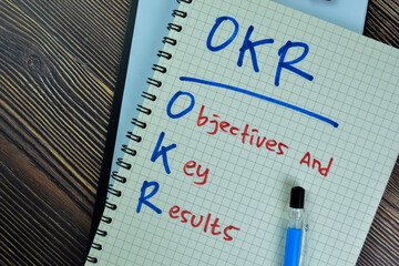 Wall Mural - Concept of OKR - Objectives and Key Results write on a book isolated on Wooden Table.