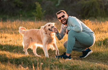 Wall Mural - Handsome man with a dog golden retriever walk in autumn meadow