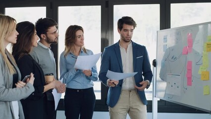 Wall Mural - Video of handsome businessman pointing at white blackboard and explain a project to her colleagues on coworking place.