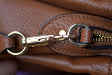 one yellow metal latch with a ring on the strap of a brown leather bag