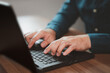 © ParinPIX - Closeup image of a young man working and typing on laptop computer keyboard on wooden table in cafe.