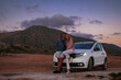 © Scopio - Man and woman sitting on hood of 3-door hatchback