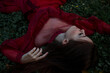 © Scopio - Mature woman in red dress laying in ground in the woods