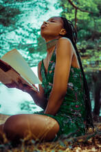 Portrait Of Young African Woman In Green Dress Holds A Book And Sitting In A Forest