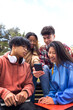 © Daniel - Multiracial happy young college student friends look at mobile phone. Teenagers using smartphone outdoor. Vertical.