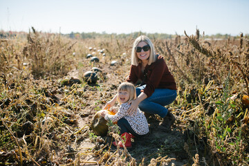 mother and daughter smiling and picking out a pumpkin together in a pumpkin patch