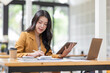 © David - Asian businesswoman working in the  workplace Office, Her is using touchpad while reading an e-mail on laptop and taking notes on the paper, accounting, tax, Financial, Business concept