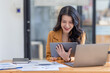 © David - Asian businesswoman working in the  workplace Office, Her is using touchpad while reading an e-mail on laptop and taking notes on the paper, accounting, tax, Financial, Business concept