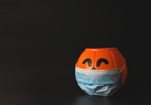 Plastic Halloween Pumpkin Wearing Medical Face Mask  On Black Background With Copy Space. New Normal  Halloween Concept