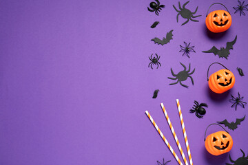 Wall Mural - Flat lay composition with plastic pumpkin baskets, paper bats, spiders and cocktail straws on purple background, space for text. Halloween decor