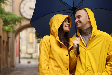 Poster - Lovely young couple with umbrella walking under rain on city street