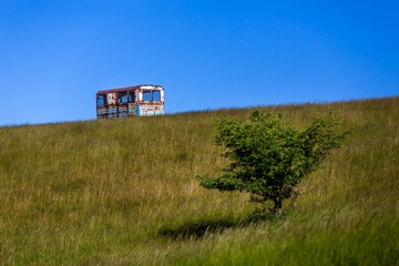 Wall Mural - Old rusty metallic cabin on the hill with dry grass against a blue sky