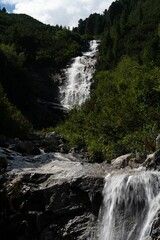 Vertical low-angle of a waterfall with trees and stone on both sides and sky background