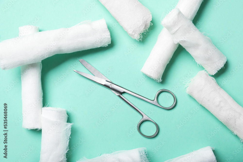 Surgical scissors and gauze rolls on color background