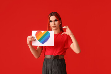 Poster - Stylish transgender woman holding paper sheet with rainbow heart against red background