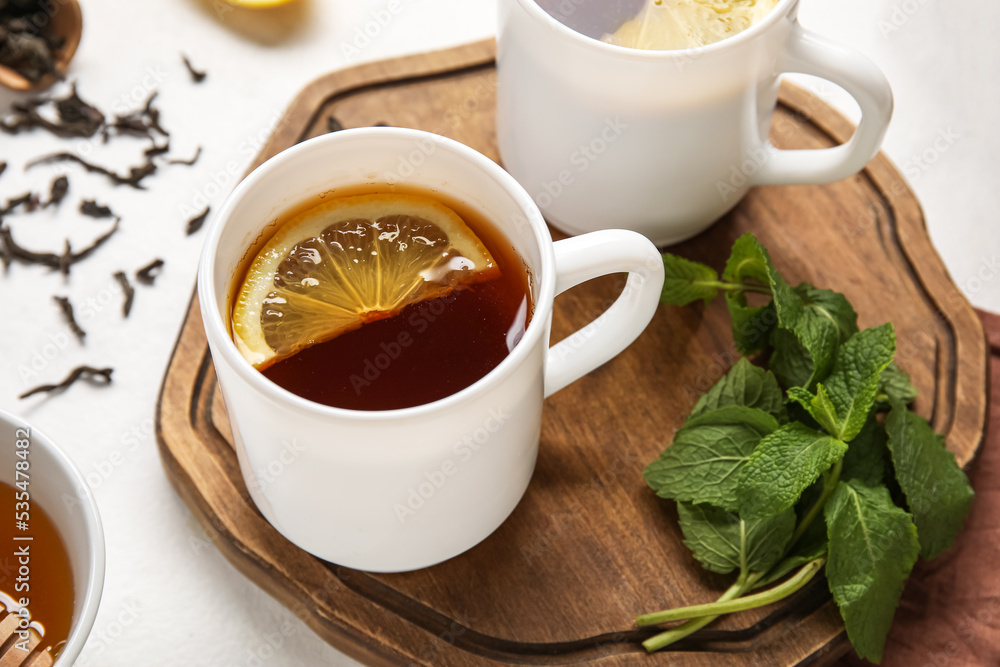 Board with cup of black tea, lemon and mint on white background, closeup
