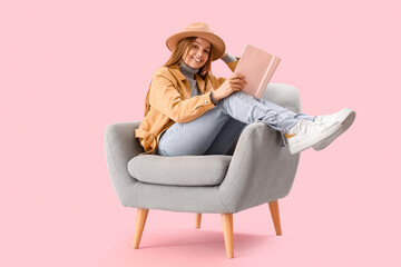 Poster - Young woman with book sitting in armchair on pink background